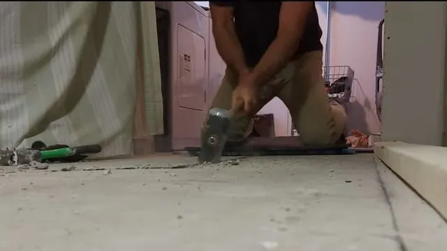 Man in a utility room swinging a hammer at a concrete slab floor to open it