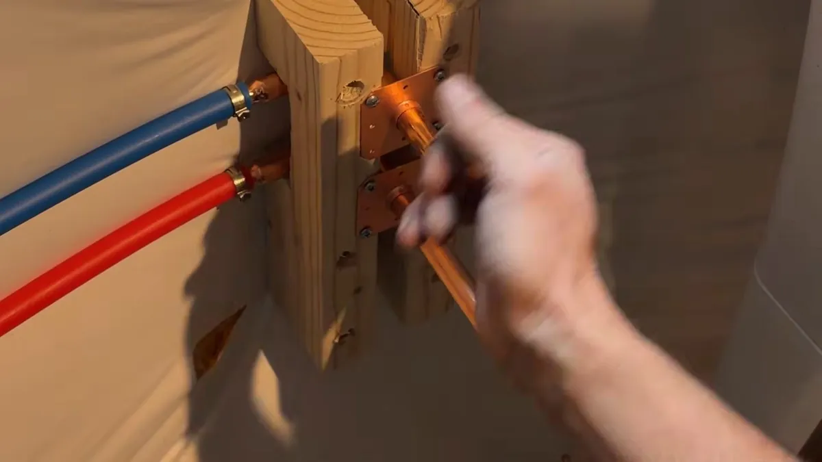 Hand adjusting red and blue PEX lines clamped to a wooden block with copper stub fittings