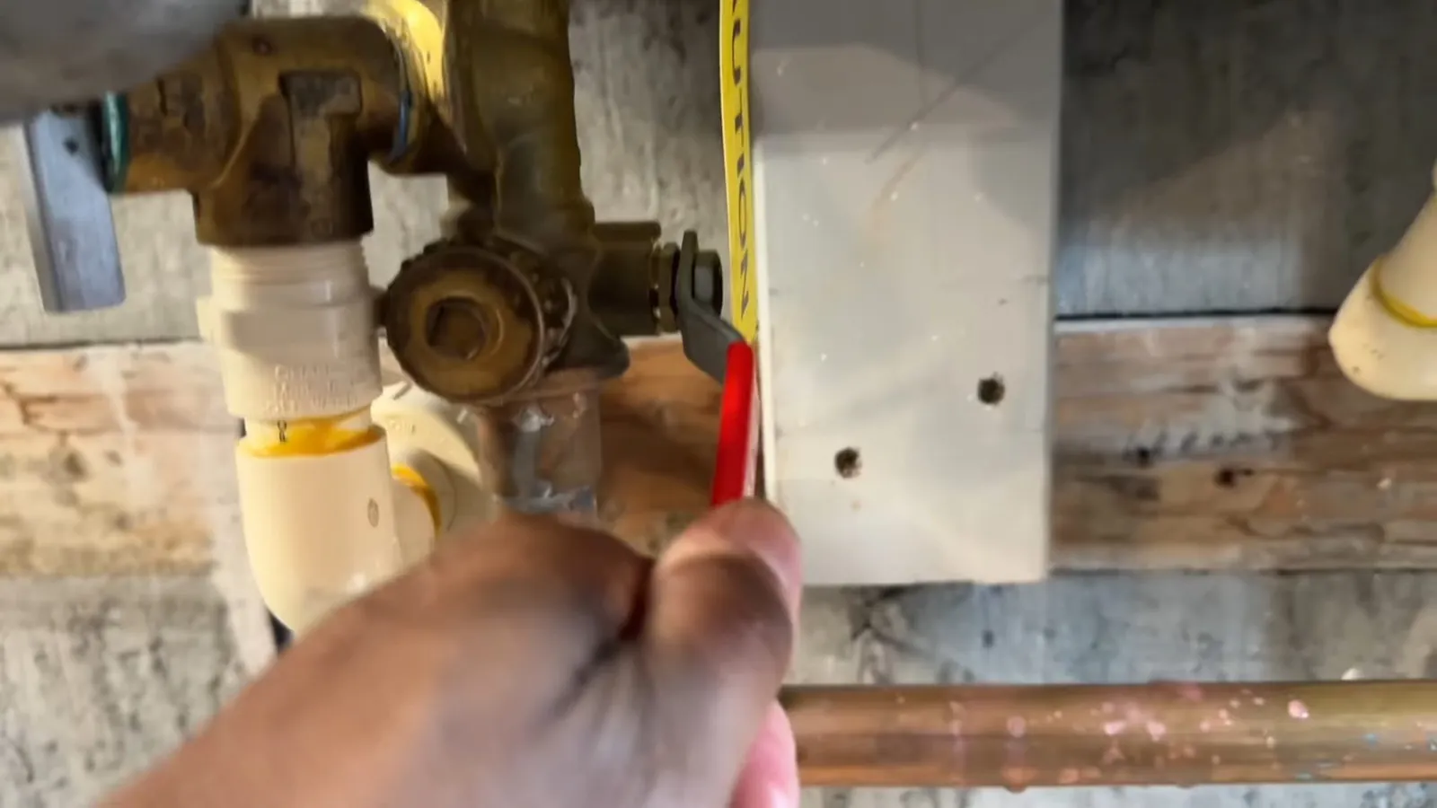 Hand holding a tape against a brass shower valve body roughed in beside plastic drain pipe
