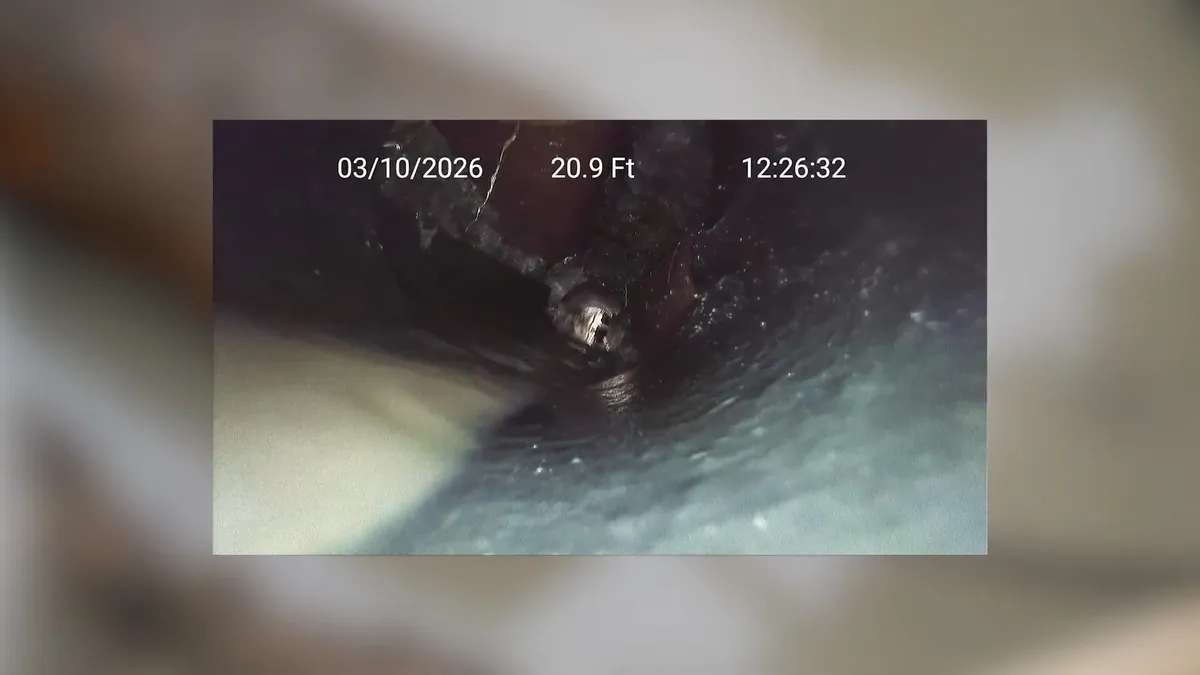 Dated camera footage from inside a pipe showing the dark bore and a fitting ahead