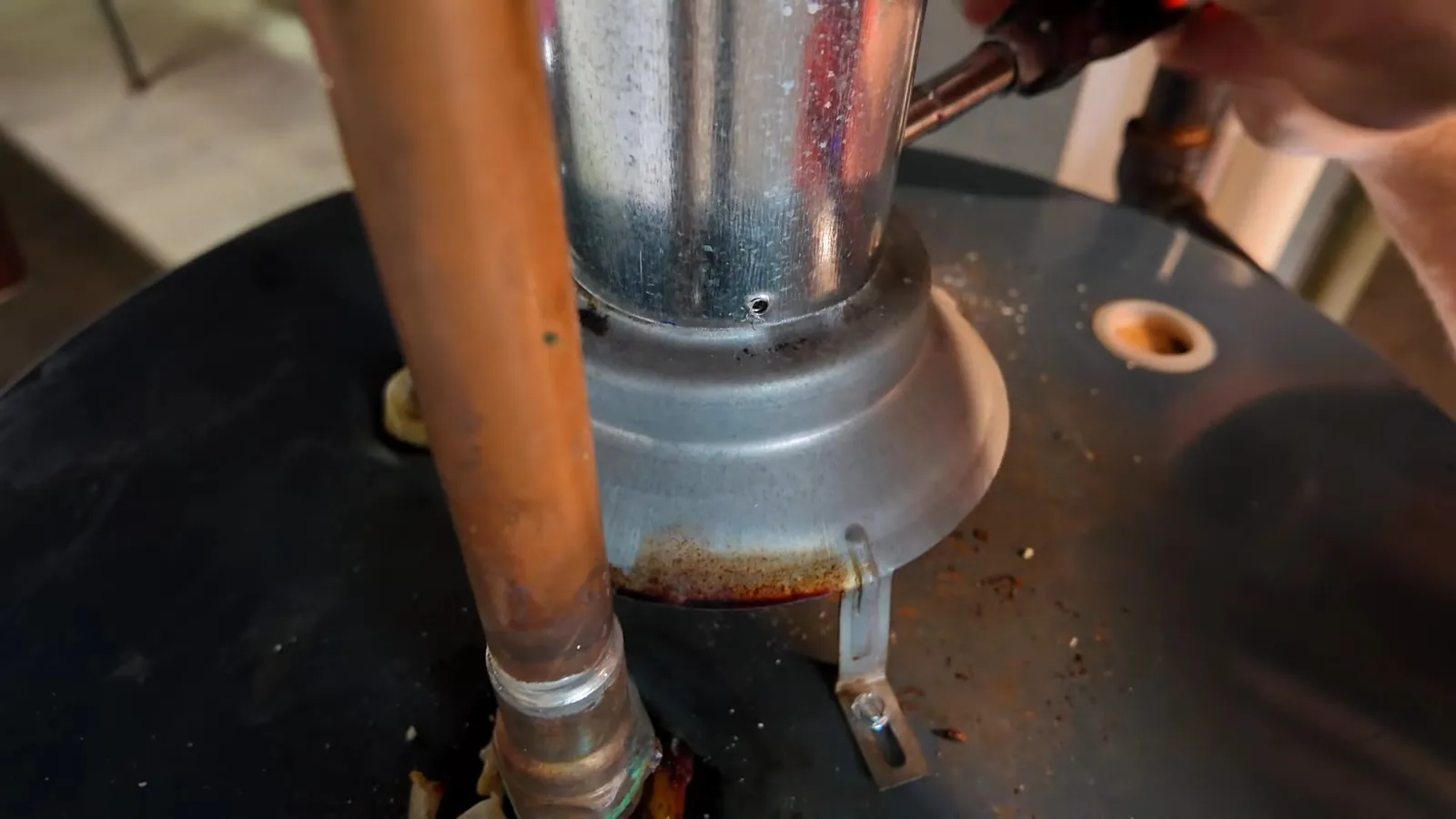 Top of a tank water heater with a galvanised vent pipe and a copper supply line rising from it