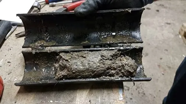 Cut-open black drain pipe holding a thick plug of sludge along its length
