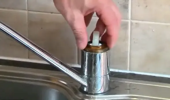 Hand lifting a brass cartridge out of a chrome single-handle tap over a steel sink