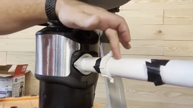 Hands fitting a white waste pipe to the discharge of a stainless garbage disposal