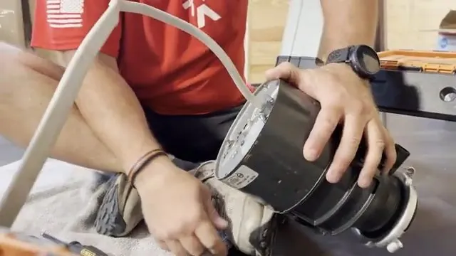Man in a red shirt holding a black garbage disposal motor unit with its power cord