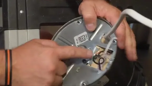 Finger pointing at the wiring and plate on the underside of a garbage disposal held in both hands
