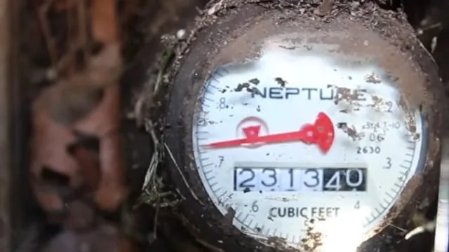 Close view of a water meter dial with the red leak indicator and the cubic feet reading