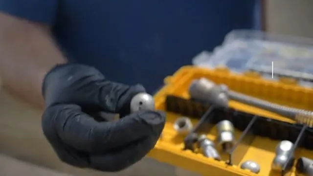 Gloved hand holding a small jetting nozzle above a yellow case of different nozzle heads