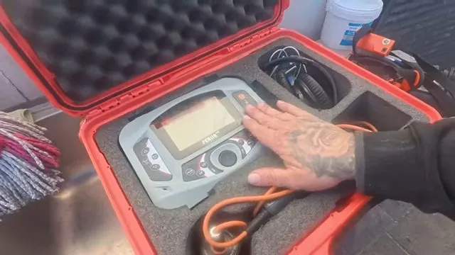 Hand resting on an electronic locator unit in an open red case with leads coiled beside it