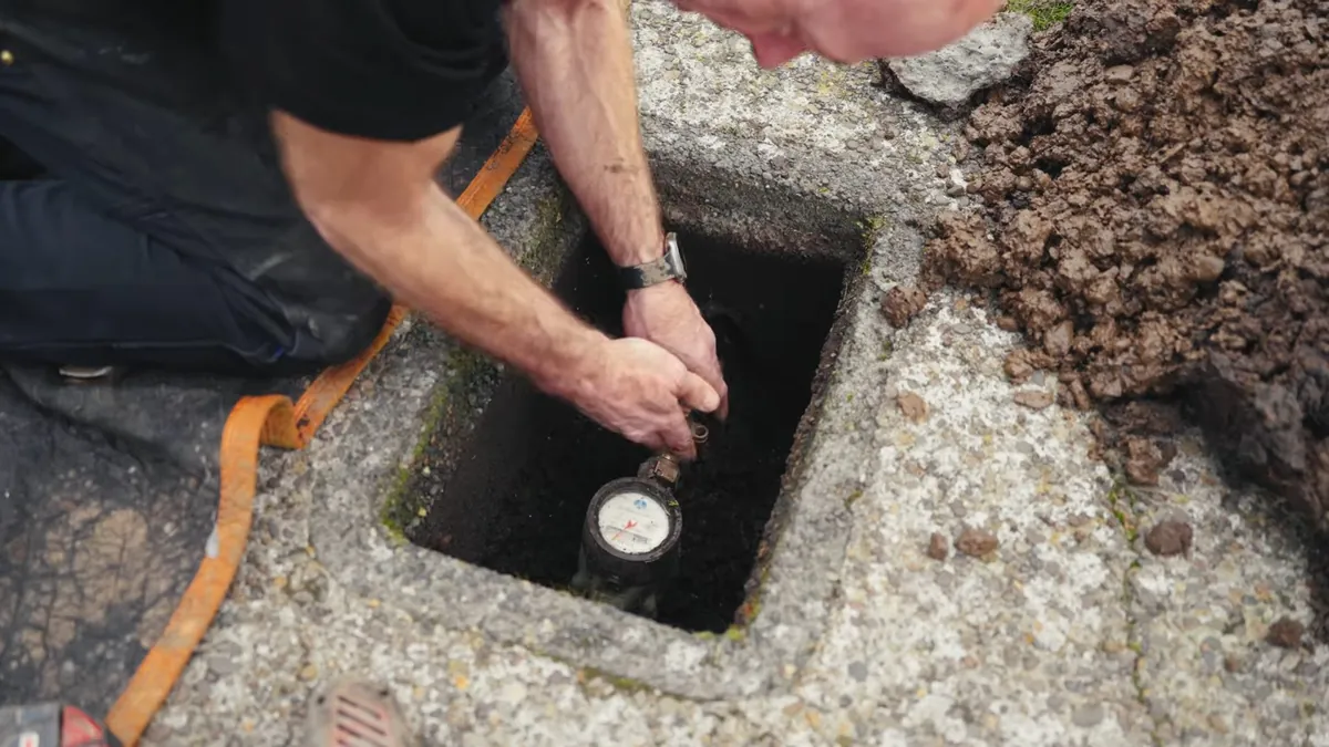 Man crouched at a ground-level meter box reaching in to read the water meter