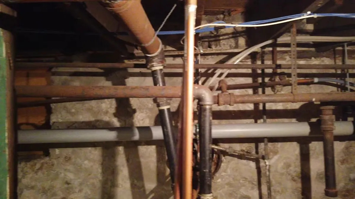 Copper, iron and plastic pipes running between floor joists in an underfloor space