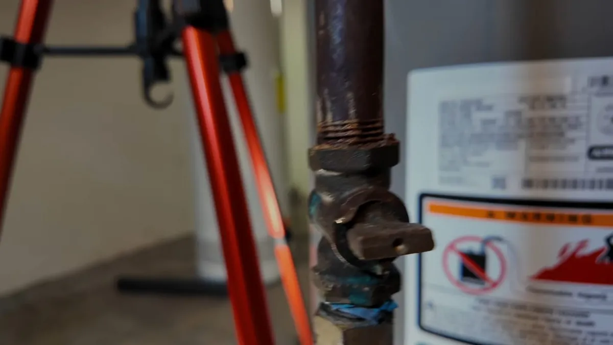 Black iron gas pipe with a lever shut-off valve beside a water heater carrying a flammable vapour warning label