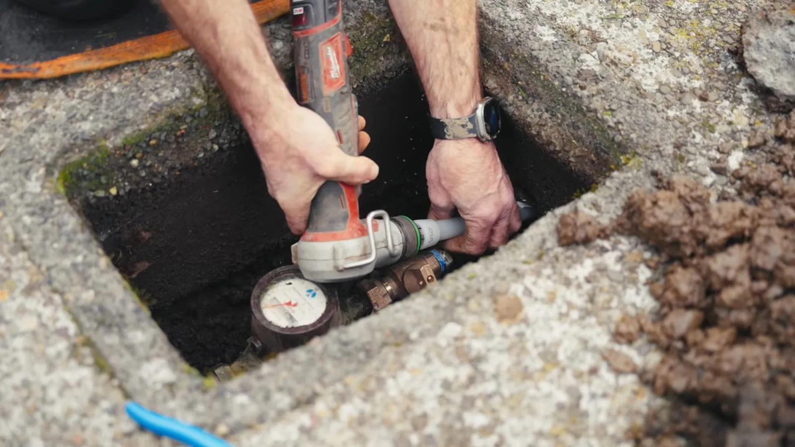 Man working with a tool at a water meter in a ground-level concrete box