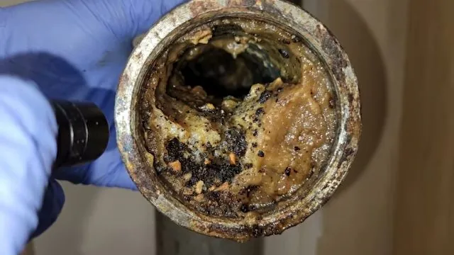 Gloved hand and torch looking into the end of a corroded pipe packed with scale and deposits