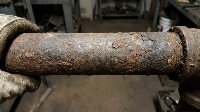 Gloved hands holding a heavily rusted length of iron pipe with a coupling at the end