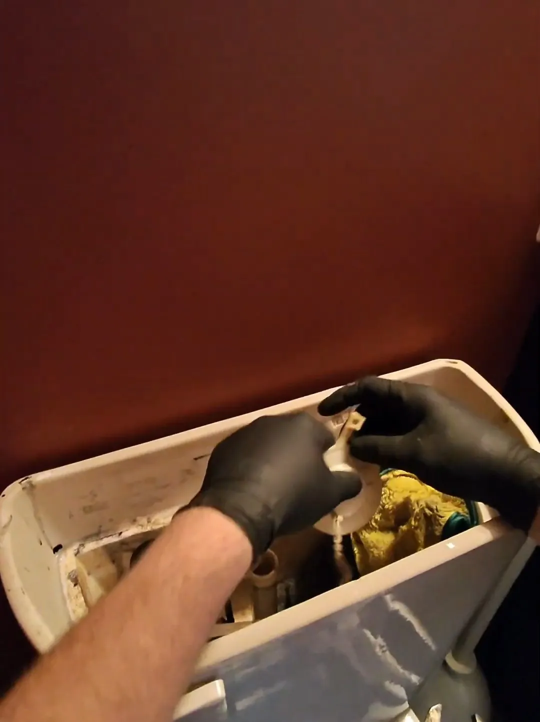 Gloved hands working on the parts inside an open toilet cistern
