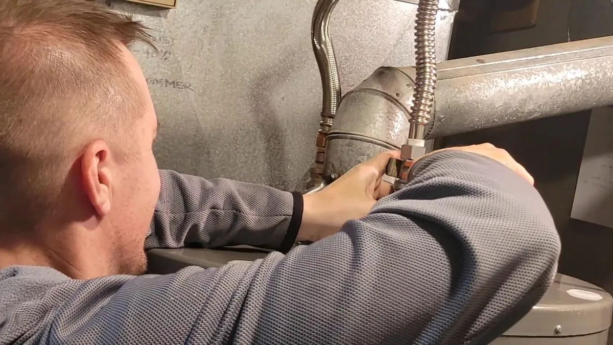 Man reaching behind a water heater to connect a braided stainless steel flexible supply line