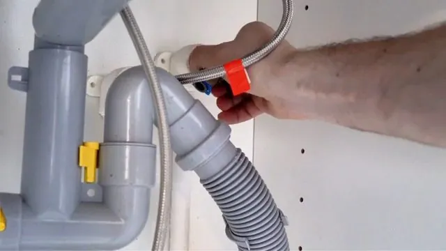 Hand holding a flexible hose beside a grey P-trap and waste pipe under a sink