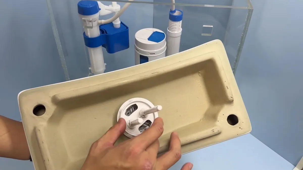 Hands fitting a flush valve seat into the bottom of an upturned beige ceramic toilet tank