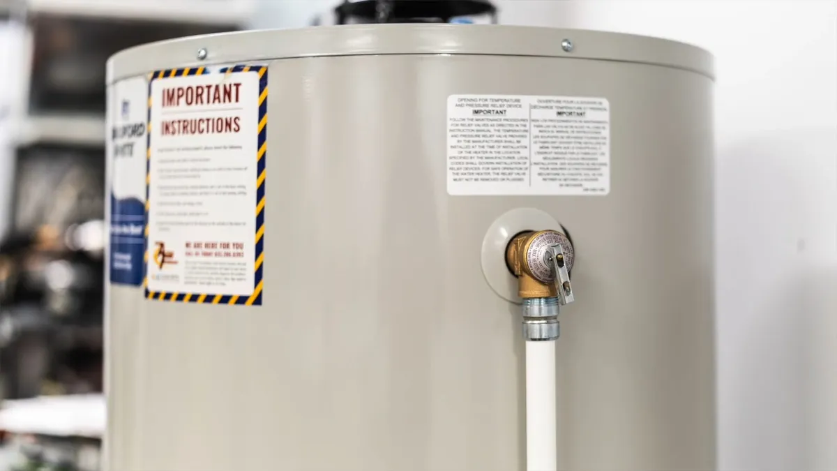 Water heater with its warning label and a white relief discharge pipe on the side