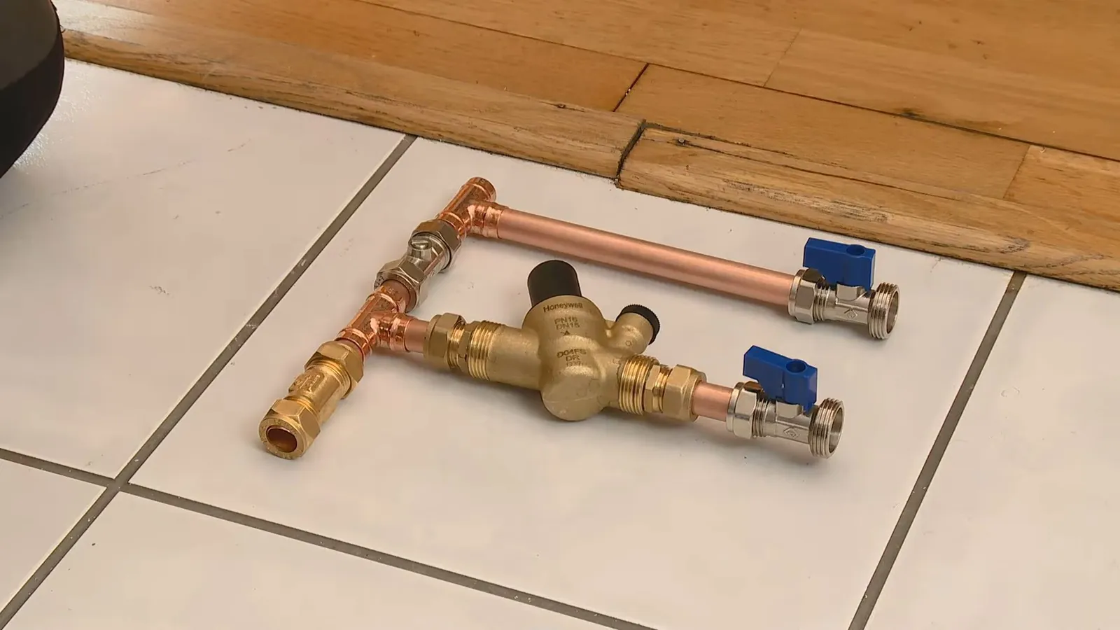 Copper assembly with two blue-handled ball valves and a pressure regulator laid on a tile floor