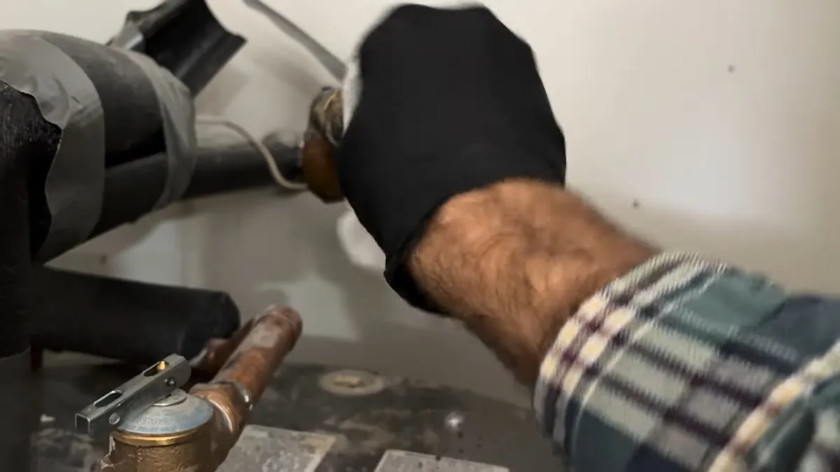 Gloved hand on a brass valve on a copper supply line, with insulated pipework beside it