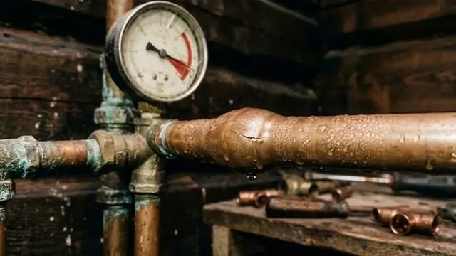 Round pressure gauge fitted to a copper supply line with fittings and tools laid out on a bench below