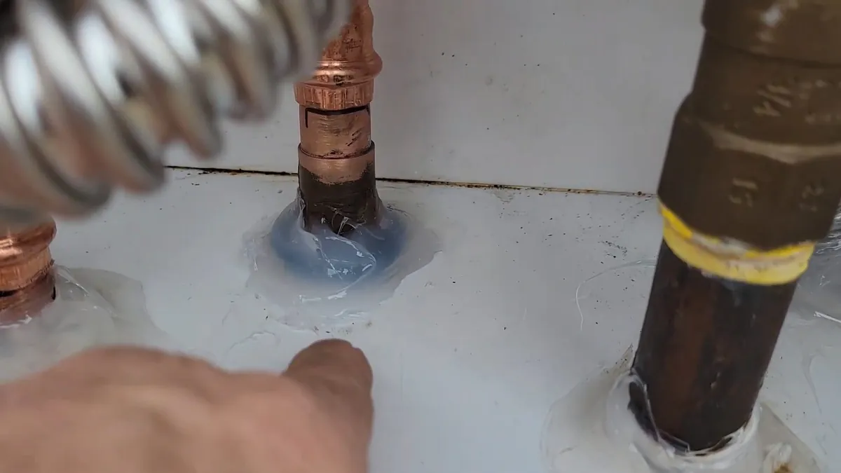 Hand pointing at the top of a tank water heater where the copper water connections and the gas pipe come in