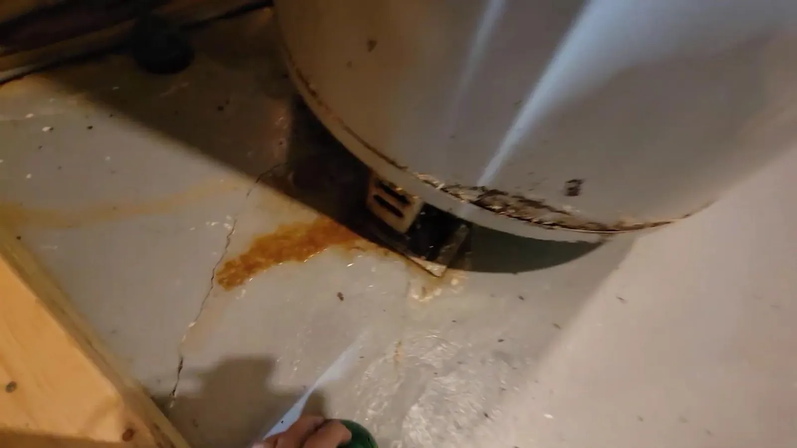 Orange rust stain and a hairline crack in a concrete floor beside the base of an old water heater