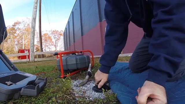 Technician at an open cleanout with a sewer camera cart beside them