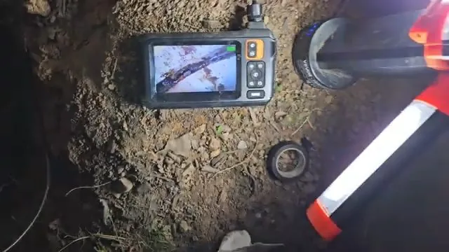 Small camera monitor on the ground beside an open pipe access with a reflective marker