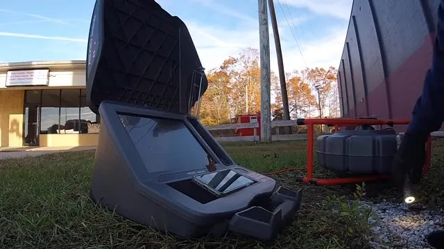 Sewer camera case open on grass with a cable reel behind it, beside a commercial building