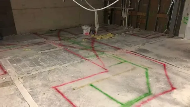 Red and green painted lines marking pipe runs on a bare concrete floor in a stripped room