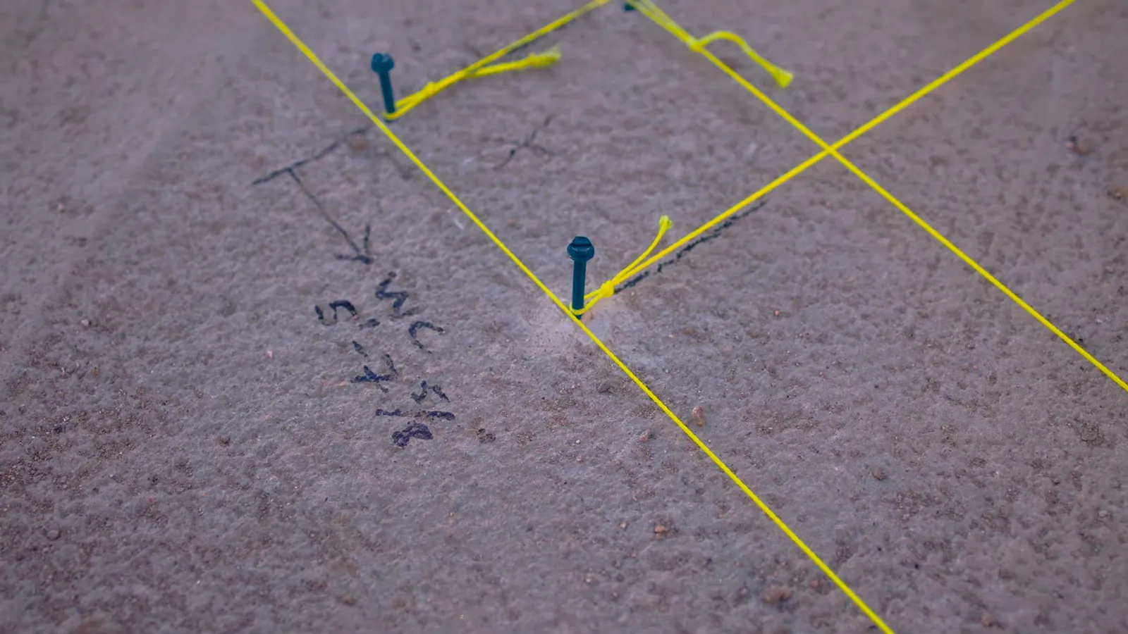 Yellow marking lines, blue pins and handwritten notes on a carpeted floor