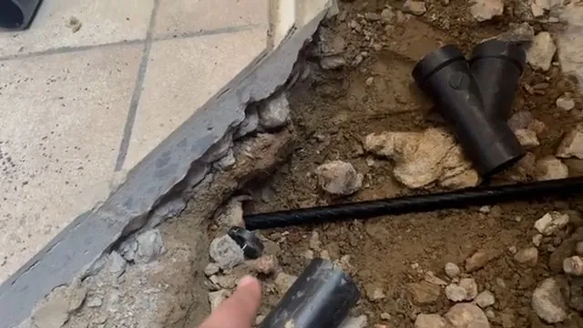 Opened concrete slab edge with a black wye fitting and pipe lying in the soil beneath