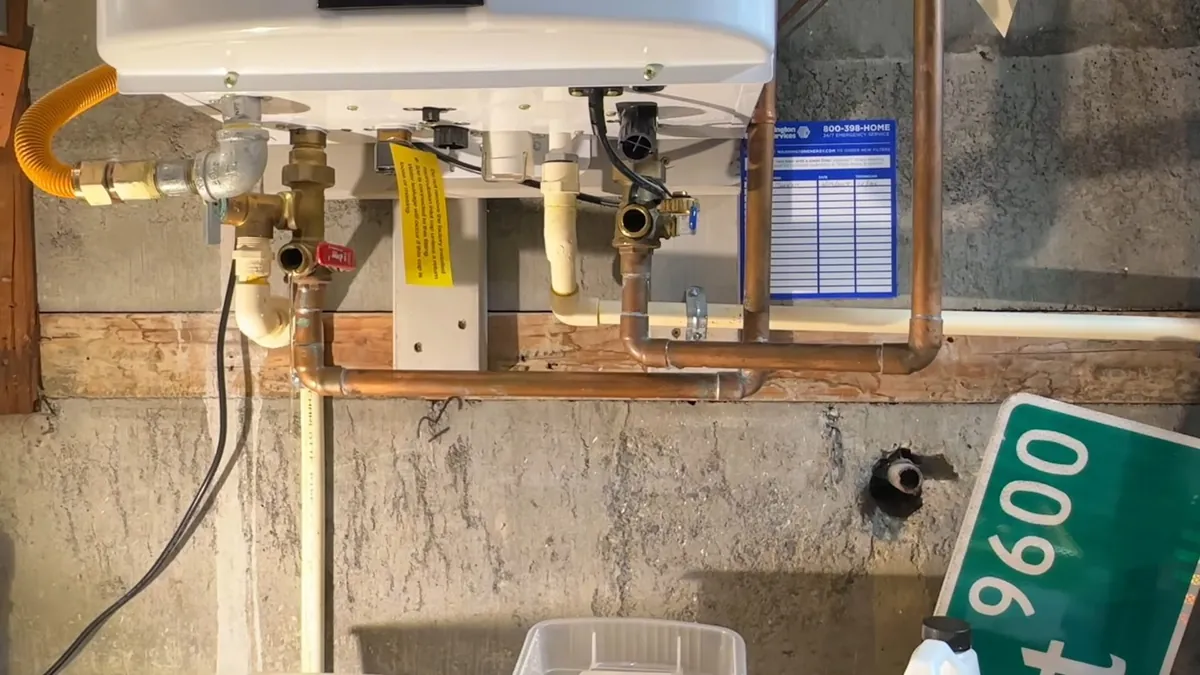 Underside of a wall-mounted tankless heater with isolation valves, a yellow gas connector and copper pipes