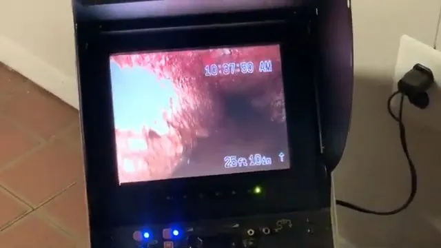 Monitor showing a red-pink view down the inside of a pipe with a depth reading