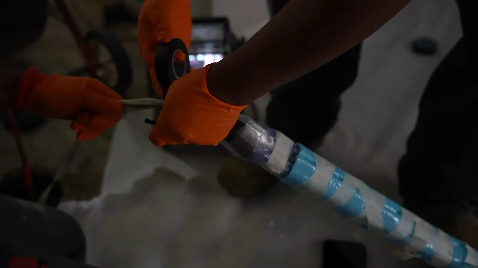 Hands in orange gloves feeding a blue and white striped liner tube into a pipe