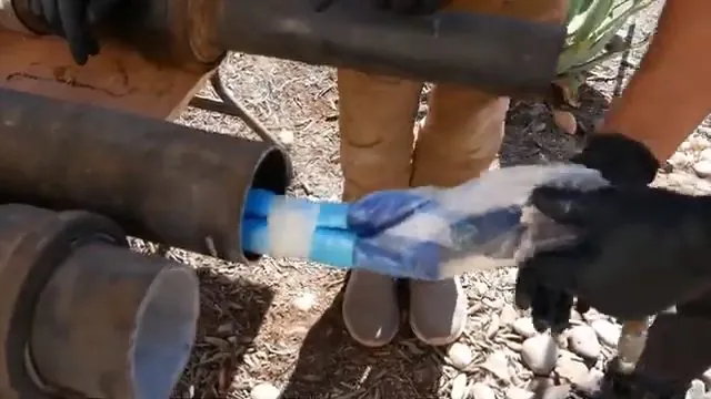 Gloved hands fitting a blue liner sleeve into the end of a large steel pipe
