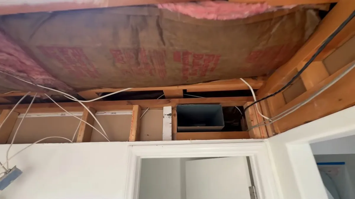Ceiling opened up between joists, showing pink insulation, electrical cable and a duct opening above a door frame