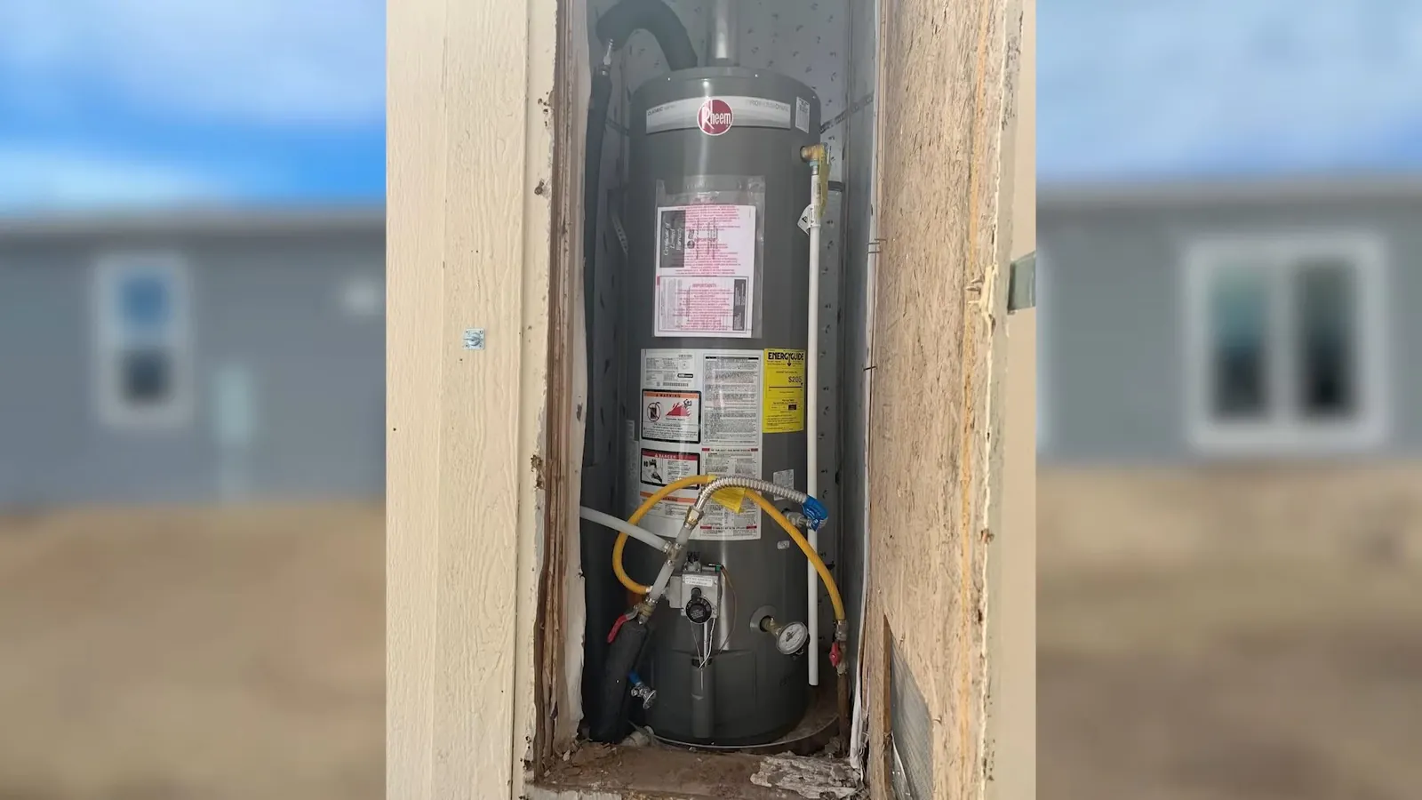 Gas water heater standing in a narrow wall alcove with yellow gas flex, in a house under construction