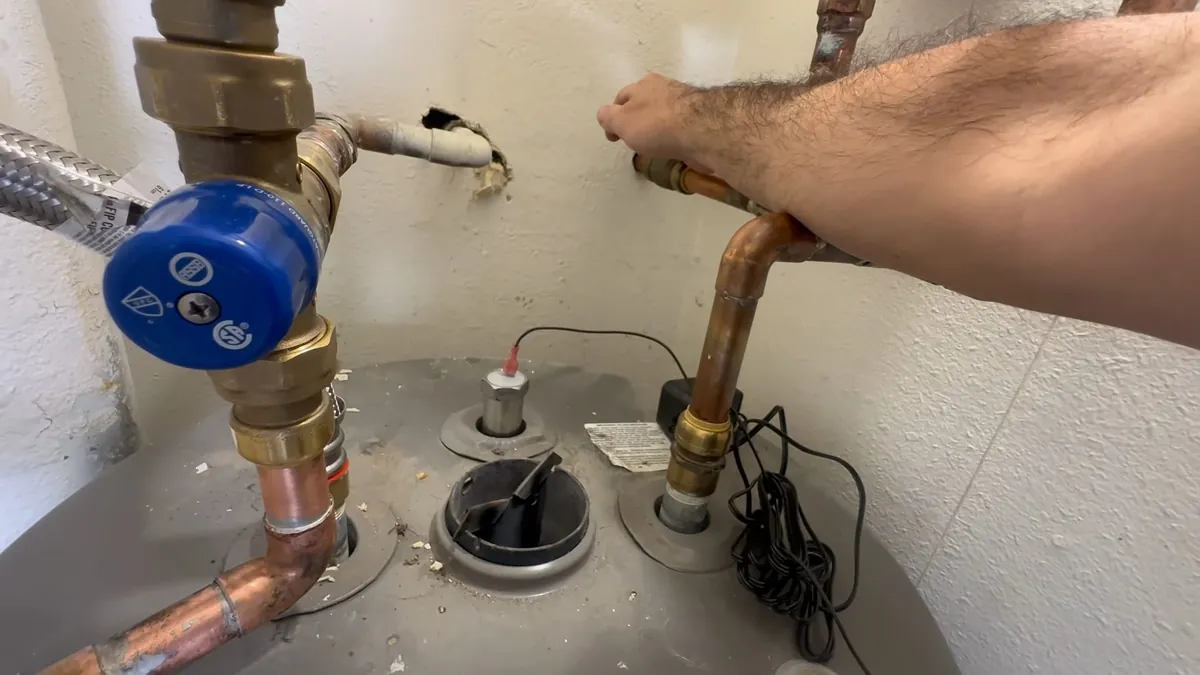 Blue-handled cold inlet valve and copper connections on top of a tank water heater